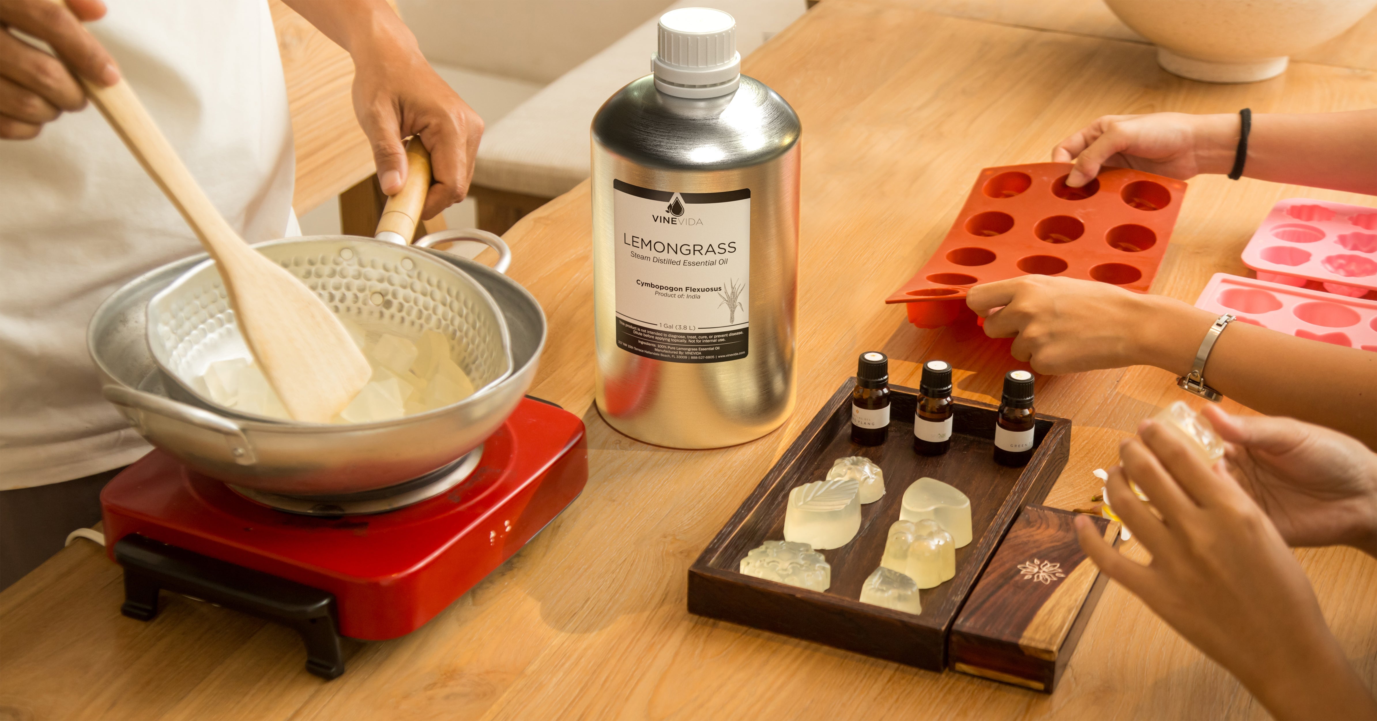 Hands pouring soap mixture into pot with essential oils and soap molds on a work surface
